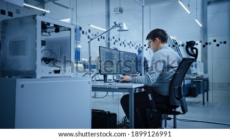 Factory Office: Portrait of Beautiful and Confident Male Industrial Engineer Working on Computer, on Screen Industrial Electronics Design Software. High Tech Facility with CNC Machinery Royalty-Free Stock Photo #1899126991