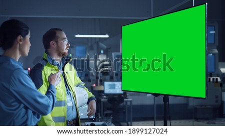 Office Meeting: Confident Female Project Manager to Chief Engineer, Watching Interactive Digital Whiteboard TV that Shows Green Screen Chroma Key Display. Factory with Machinery.