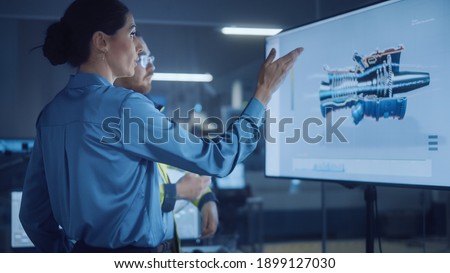 Office Meeting: Female Manager Talks to Male Engineer, Watching Interactive Digital Whiteboard TV that Shows New Sustainable Eco-Friendly Engine 3D Concept. Modern Factory.