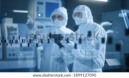 Factory Cleanroom: Engineer and Scientist Wearing Coveralls, Standing in Workshop Talk and Use Tablet Computer, Professionals Develop Technology for Modern CNC Machinery and Electronic Equipment Royalty-Free Stock Photo #1899127090