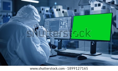 Research Factory Cleanroom: Close-up of Engineer Scientist wearing Coverall and Gloves Uses Microscope, Computer Has Chroma Key Green Screen Display. Scientific and Electronics Research Facility