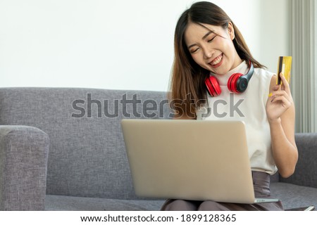 A young Asian woman holds a credit card and uses a laptop to shop online in the office at home. Work from home concept.