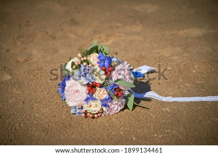 a luxurious wedding bouquet made of colorful flowers and berries tied with lace ribbon lying on the sand of the beach