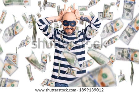 Young handsome man wearing burglar mask posing funny and crazy with fingers on head as bunny ears, smiling cheerful