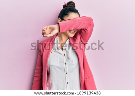 Beautiful middle eastern woman wearing business jacket and glasses covering eyes with arm smiling cheerful and funny. blind concept. 