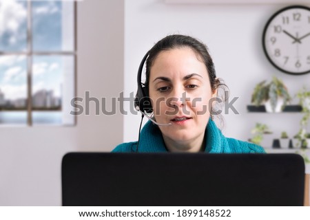 Young caucasian female employee tele-working in the livingroom at home. Headphones and video call talk. Empty copy space for Editor's content.