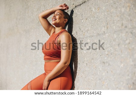 Woman with plus size body leaning to a wall and relaxing after workout session outdoors. Woman in sports clothing taking a break from exercise. Royalty-Free Stock Photo #1899164542