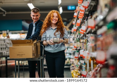 Two young workers working in a supermarket. Man and woman supermarket employees at work stocking up the product shelves.
