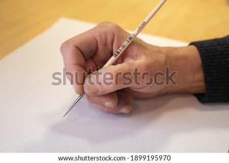 The artist begins to paint a picture. Artist's hand with a paintbrush on a white sheet background. The hand of the old master.