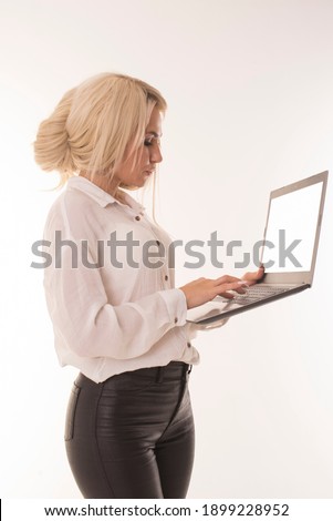 Blonde woman with a laptop in her hands stands and works. Girl in a shirt works at a laptop in the studio. 