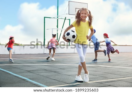 Cute girl with soccer ball at sports court on sunny day. Summer camp
