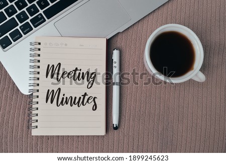 Top view of laptop, pen and notebook written with text MEETING MINUTES over brown background. Business concept. Royalty-Free Stock Photo #1899245623