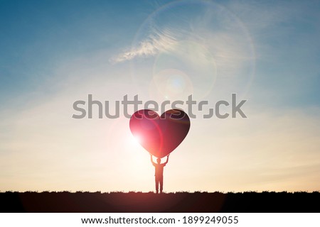 Silhouette man show two hand rise up and carrying heart with sunlight  and blue sky , Valentine 's day concept.