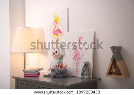 Pictures and stationery with toys on chest of drawers in children's room. Interior design