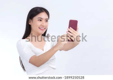 Portrait of Asian beautiful woman who has black long hair in white shirt, is holding the smartphone in her hand and smiling. She take a selfies photo on white background.