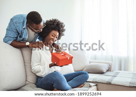 Beautiful young couple is celebrating at home. Handsome man is giving his girlfriend a gift box. Young romantic couple holding present. he guy gives a gift box to his girlfriend.