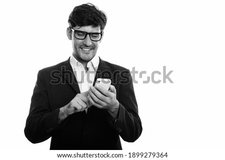 Studio shot of young happy Persian businessman smiling while using mobile phone