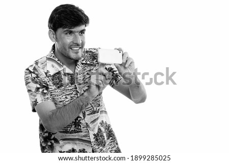 Thoughtful young happy Persian man smiling while taking picture with mobile phone