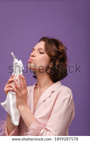 Close-up portrait of young lady isolated over violet background. Beauty and skincare concept. Pretty girl with dark short hair, wearing pink shirt, holding white silk towel