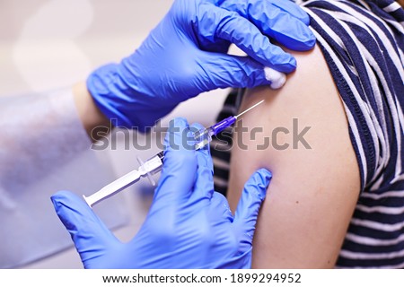 Doctor or nurse giving shot or vaccine to a patient's shoulder. Vaccination and prevention against flu or virus pandemic. Doctor in gloves holding syringe and making injection to patient. 