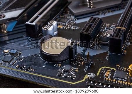 CMOS backup battery for powering BIOS settings and real-time clock circuit on a modern black motherbord. Computer mainboard circuit components. Desktop PC hardware components. Close-up.  Royalty-Free Stock Photo #1899299680
