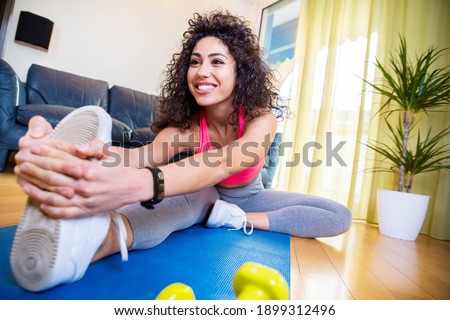 Sporty woman wearing sportswear working out at home doing stretching exercise - Young girl training fitness in the living room - Sport and recreational concept.