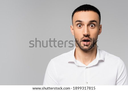 amazed hispanic manager with open mouth and bulging eyes looking at camera isolated on grey Royalty-Free Stock Photo #1899317815