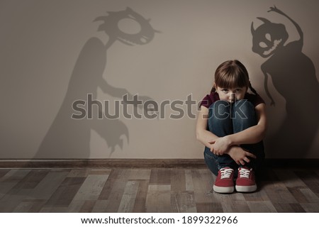 Shadows of monsters on wall and scared little girl in room