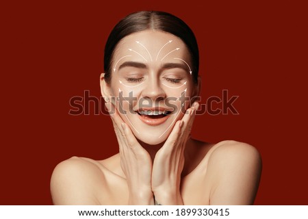 Beautiful female face with lifting up arrows isolated on red background. Concept of bodycare, cosmetics, skincare, correction surgery, beauty and perfect skin. Flyer for your ad. Antiaging. Royalty-Free Stock Photo #1899330415