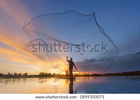 Fisherman casting his net on during sunrise.Silhouette Asian fisherman on wooden boat casting a net for freshwater fish Royalty-Free Stock Photo #1899350071