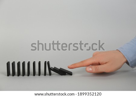 Woman causing chain reaction by pushing domino tile on grey background, closeup. Space for text Royalty-Free Stock Photo #1899352120