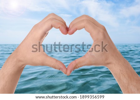 Man making heart with hands near sea on sunny day, closeup