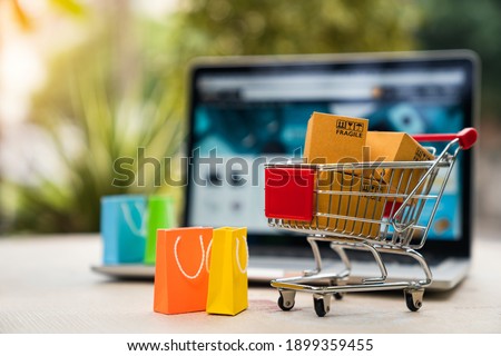 Product package boxes in cart with shopping bag and laptop computer with blurred web store shop on screen for online shopping and delivery concept Royalty-Free Stock Photo #1899359455