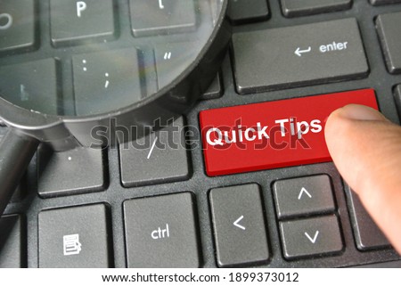 Selective focus of magnifying glass on a keyboard with red button written Quick Tips. Finger press Quick Tips button. Business and Financial concept. Content contain chrominance noise and film grain.