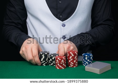 a croupier in a white vest and a black shirt is counting poker chips