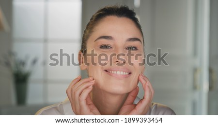 Beauty shot of mature woman with perfect face skin after applying moisturizing cream pampering it gently with fingers to absorb better on golden background. Concept of skincare, cosmetics, healthcare Royalty-Free Stock Photo #1899393454
