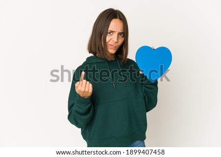 Young hispanic woman holding a heart shape pointing with finger at you as if inviting come closer.