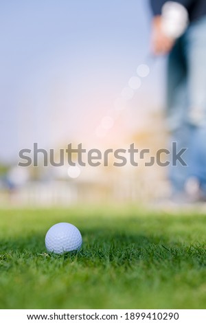 Green grass with golf ball close-up in soft focus at sunlight and have blur background with man playing golf end game successful.