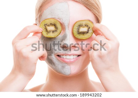 Skin care. Young woman with clay mask on her face covering eyes with slices of kiwi fruit. Girl taking care of her dry compexion. Isolated. Spa and beauty treatment.