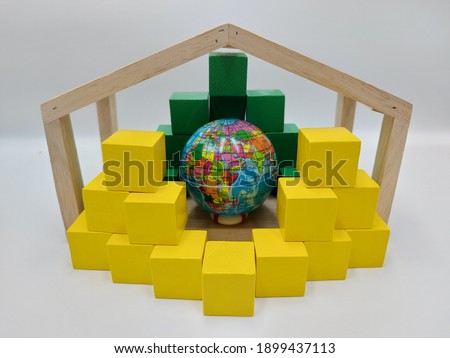 Mini plastic globe inside a wooden house shaped frame and surrounded by stacks of green and yellow blocks, to present a global framework and breakthrough