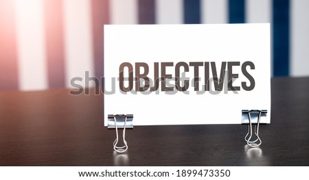 Objectives sign on paper on dark desk in sunlight. Blue and white background