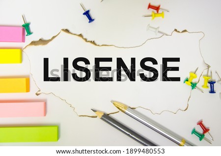 the word license is written on a white sheet of paper on a white background near a pen and a multi-colored button and stickers. High quality photo