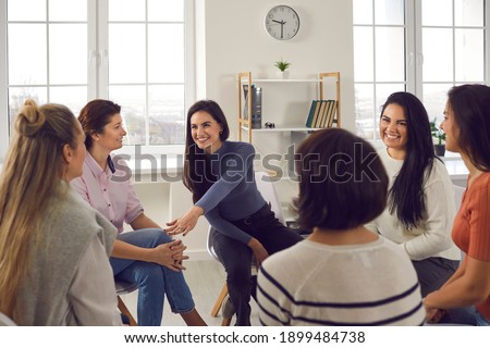 Happy positive smiling female coach, therapist or business team manager supporting and motivating young women in group therapy session or corporate staff training meeting at work Royalty-Free Stock Photo #1899484738