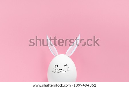 Easter egg with bunny ears and face on pink background with copy space. Flat lay or top view. Minimal concept. Conceptual creative photo approaching Happy Easter holiday