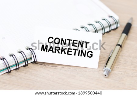 Text content marketing on a white business card, which lies on the table next to a notebook with a golden pen