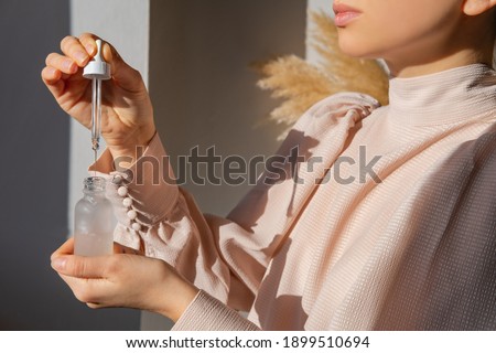 Woman in pink vintage blouse holding serum glass bottle with pipette. Hyaluronic acid, retinol. Trendy colors. Skin care routine concept. Hydrating facial moisturizer Royalty-Free Stock Photo #1899510694