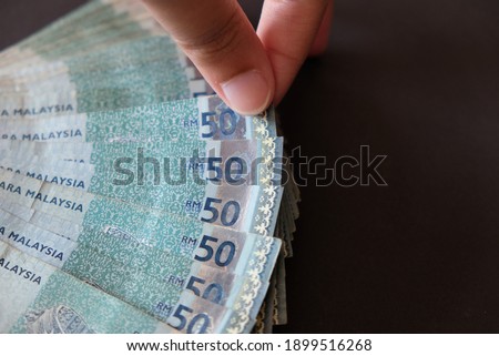 Hand holding 50 ringgit malaysia (MYR) banknote on black background. Concept for business, finance, trade, economy and investment.