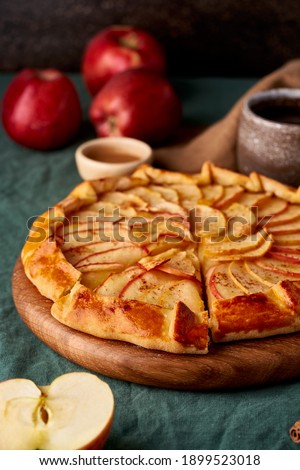 Apple pie, galette with fruits, sweet pastries on dark green tablecloth, sweet crostata on cutting wooden board, side view, autumn or winter food, vertical Royalty-Free Stock Photo #1899523018