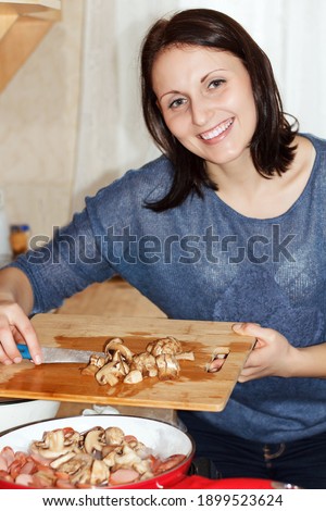 Smiling woman chef cutting a mushroom on a cutting board and throws in frying pan