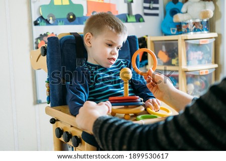 Activities for kids with disabilities. Preschool Activities for Children with Special Needs. Boy with with Cerebral Palsy in special chair play with mom at home. Royalty-Free Stock Photo #1899530617